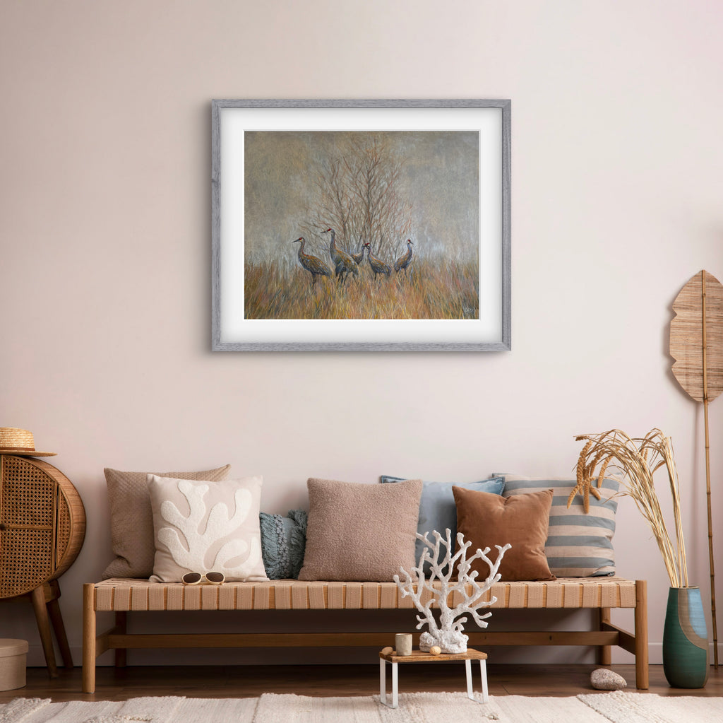 Framed artwork of cranes in a field above a living room sofa with decorative pillows.