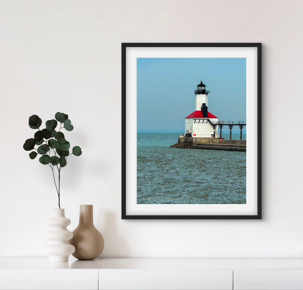 Framed picture of a lighthouse on a wall with a vase and plant below.
