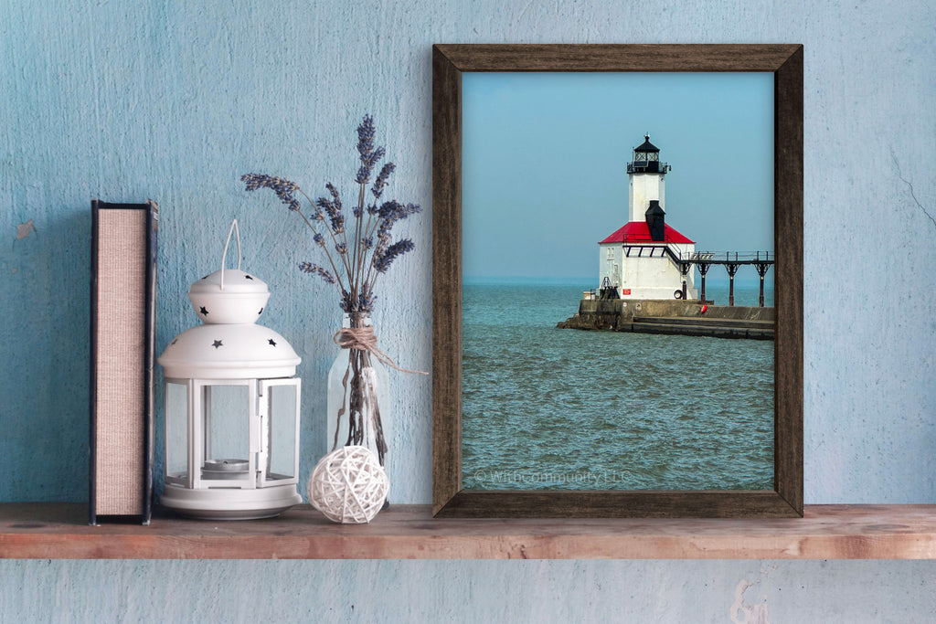 Framed picture of a lighthouse on a shelf with decorative items against a blue wall.