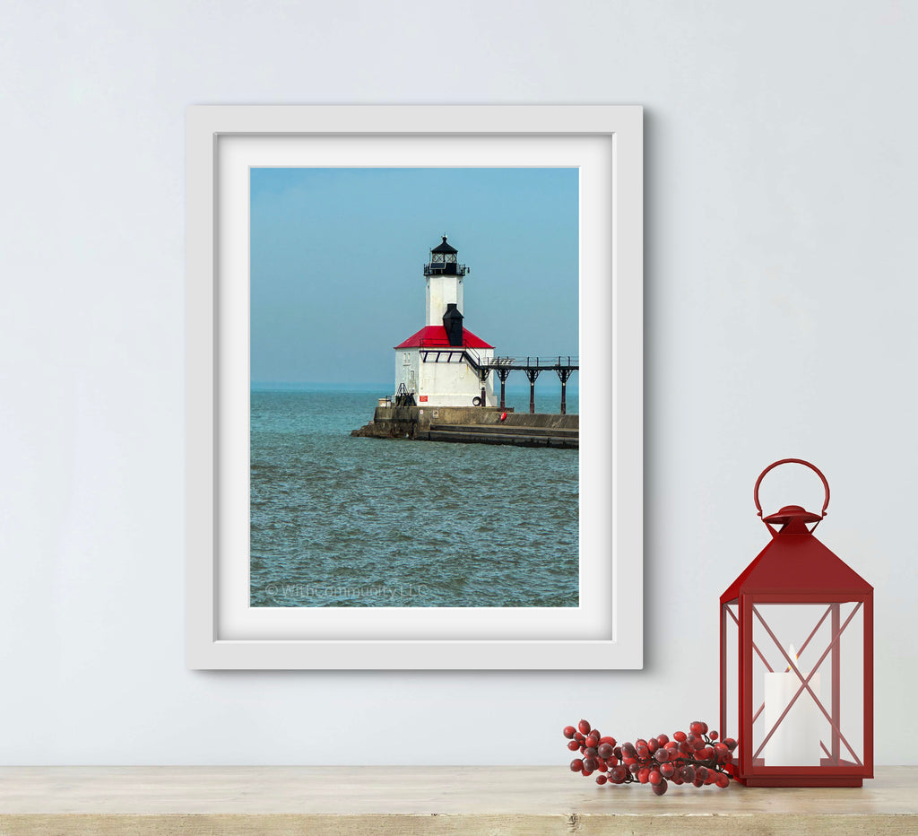 Framed photograph of a lighthouse on a wall with a red lantern and decorative branches below.