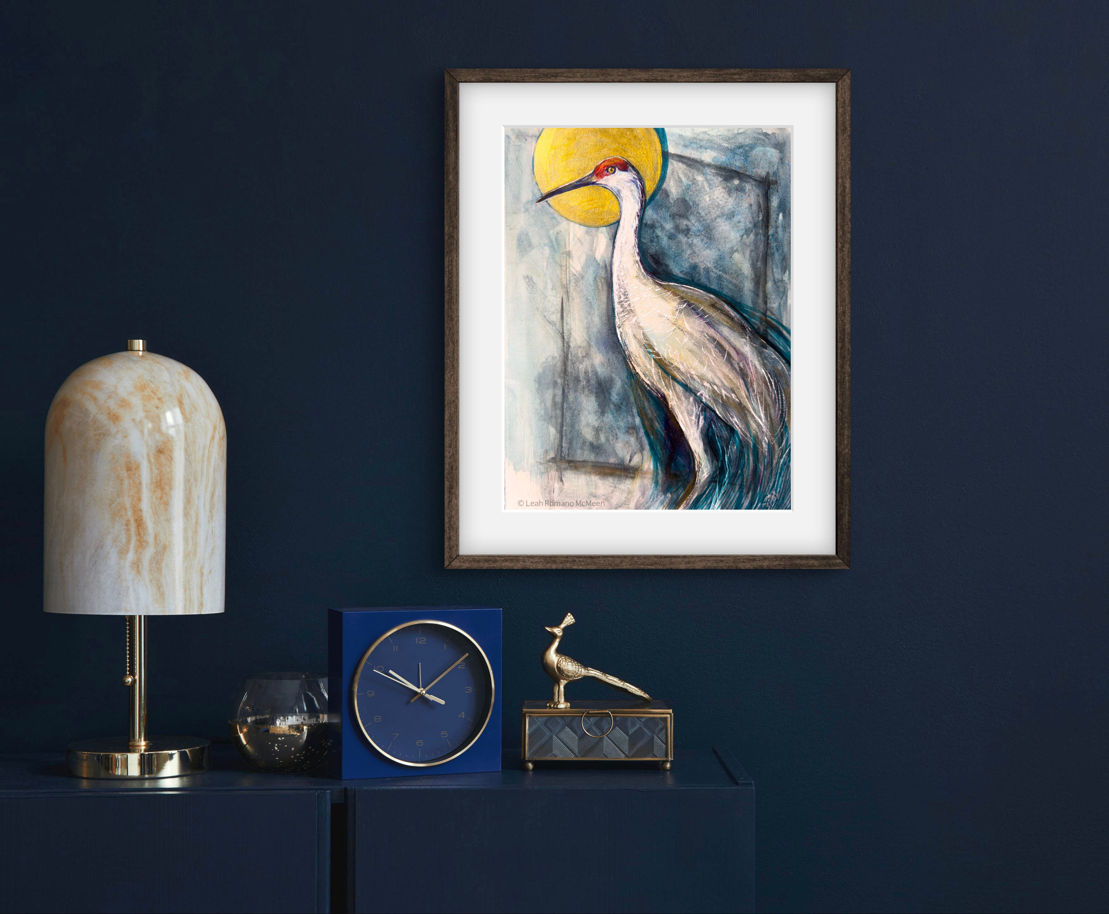 Framed artwork of a crane bird on a dark blue wall with decorative items below.