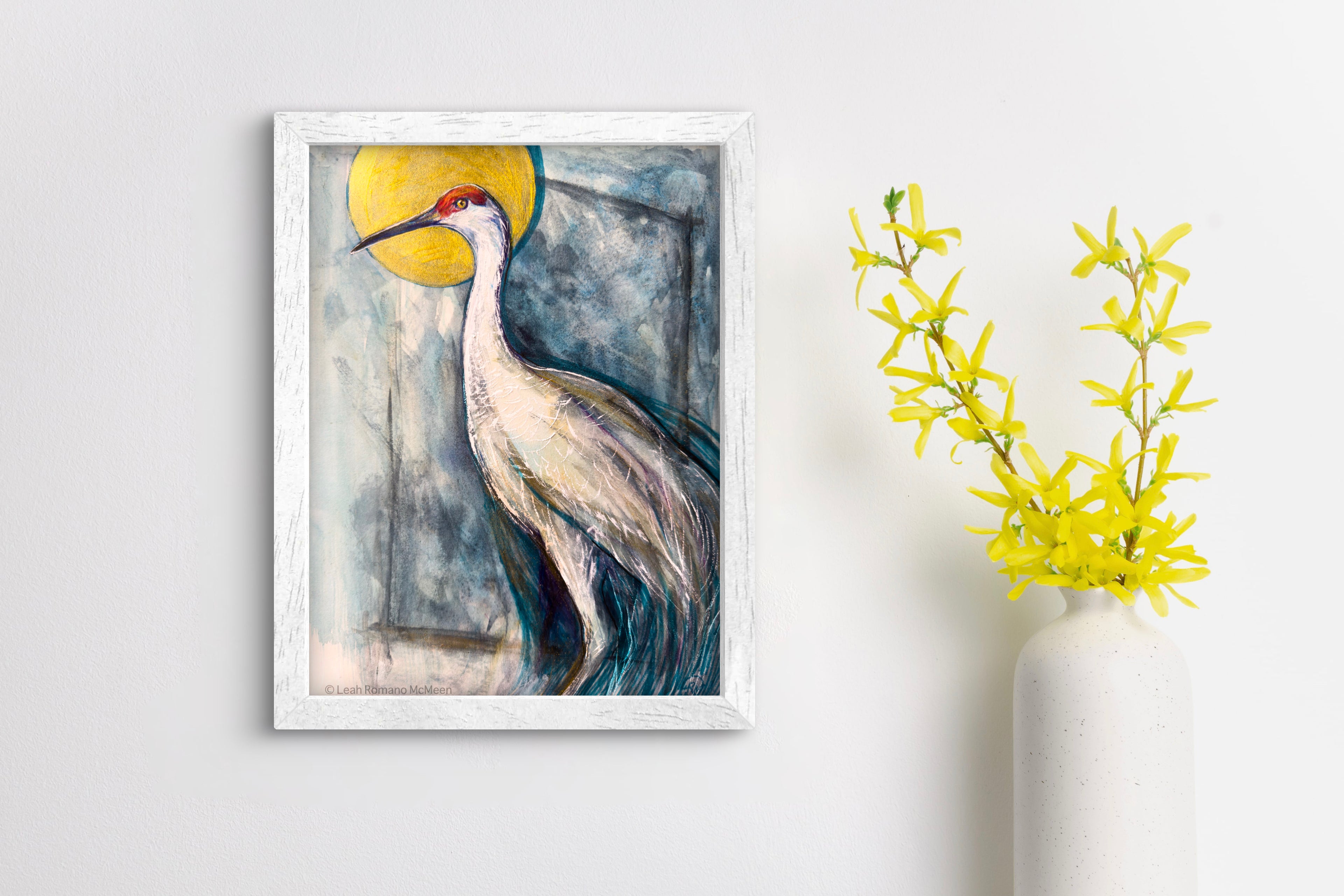 Framed artwork of a crane bird with a yellow circle on a white wall.