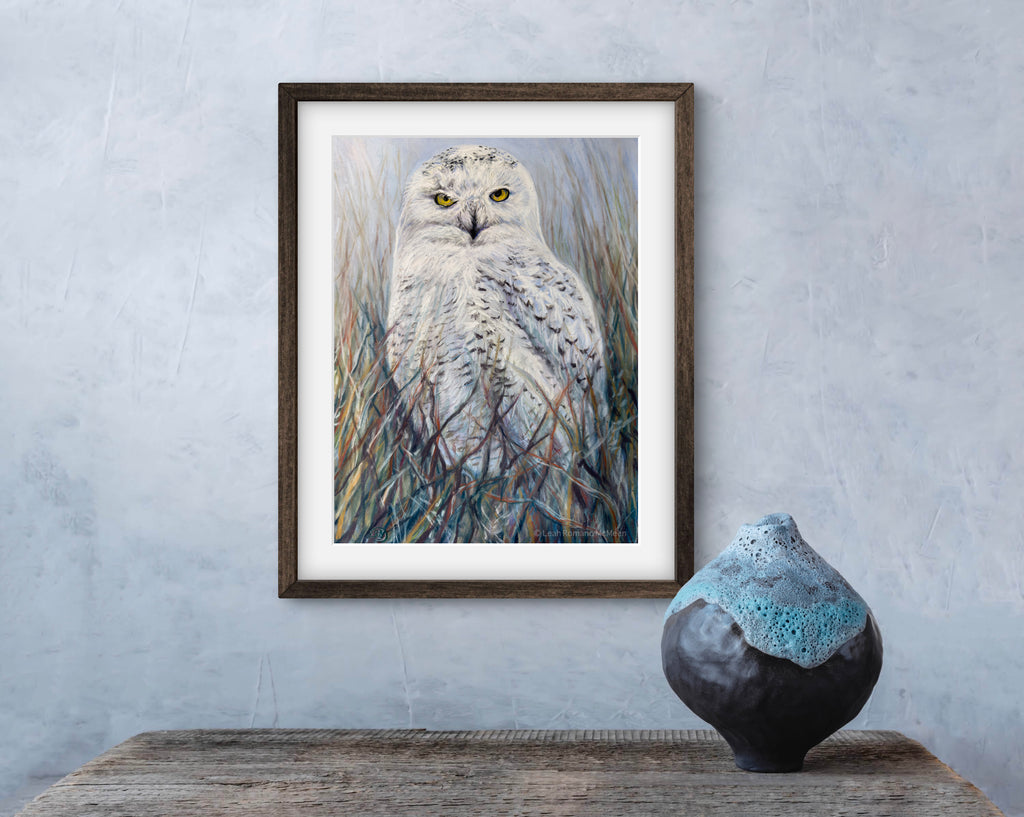 Framed artwork of an owl on a wall above a textured surface with a ceramic vase.