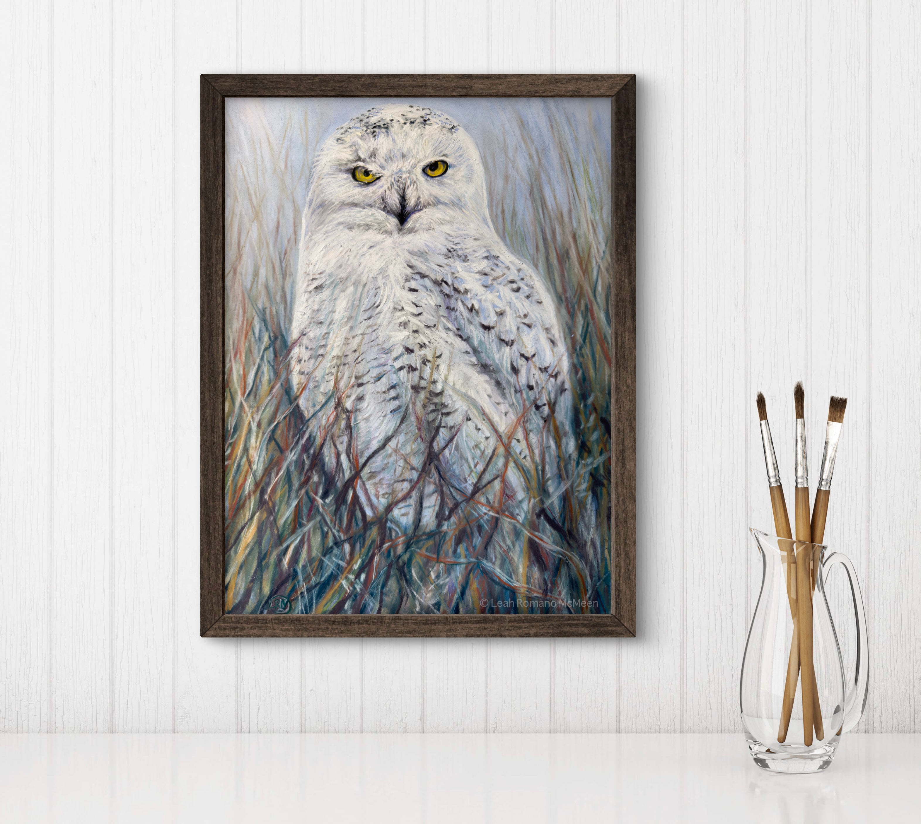 Framed artwork of an owl in a natural setting on a white wall.