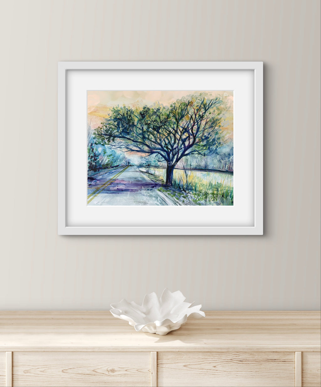 Framed artwork of a tree by on a wall above a wooden cabinet.