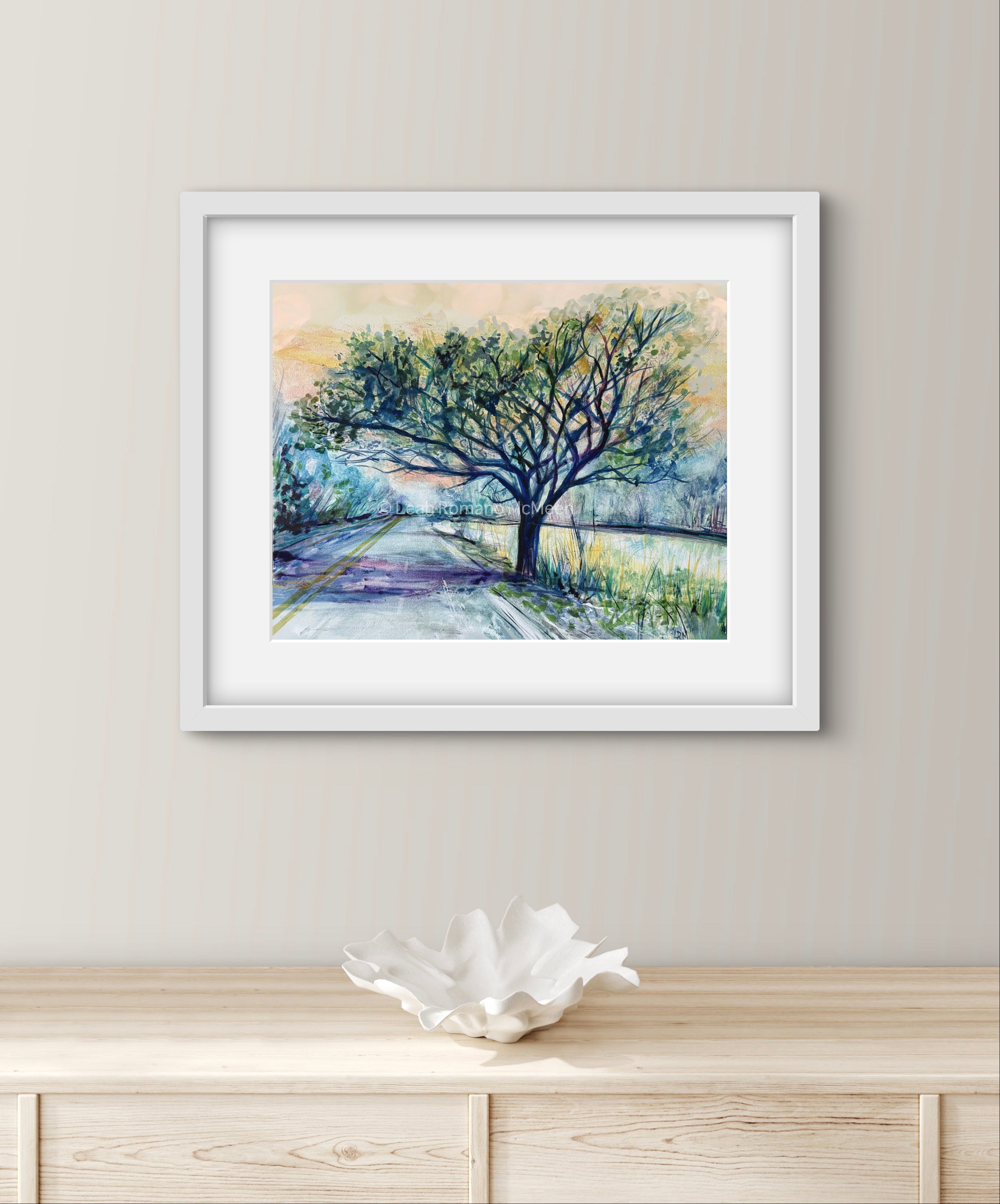Framed artwork of a tree by on a wall above a wooden cabinet.