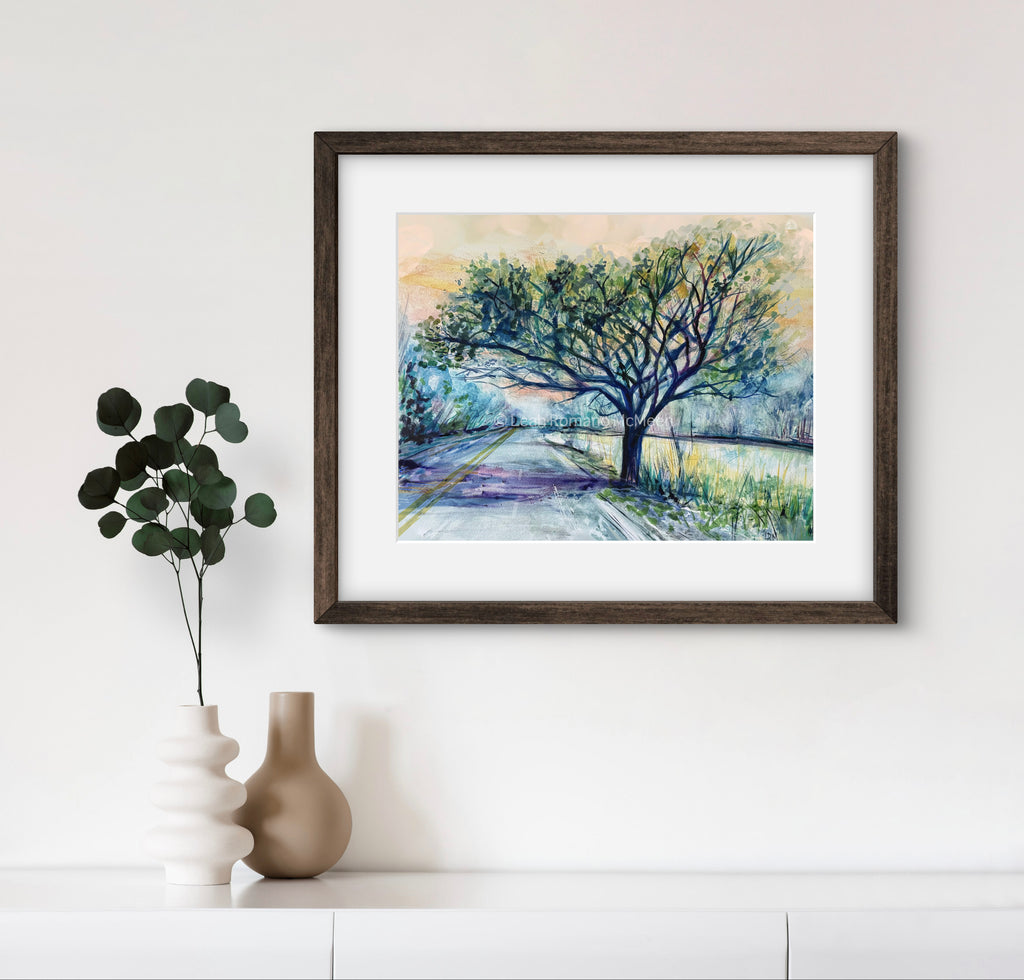Framed artwork of a tree on a path with a vase and plant on a shelf below.